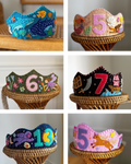 Collection of colorful children's birthday crowns with numbers and patterns on a wooden stand.