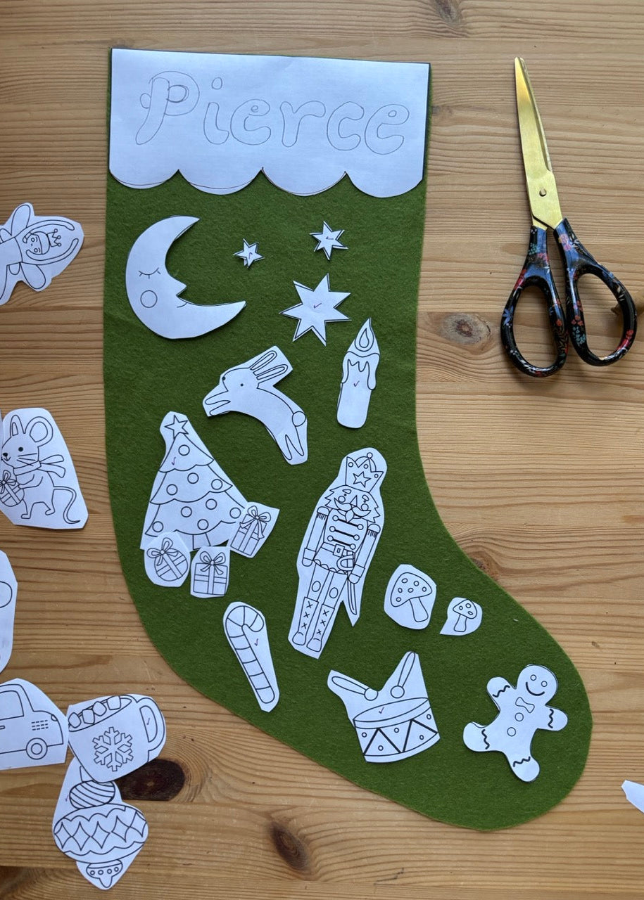 Green stocking with white cut-out decorations on a wooden surface with scissors.