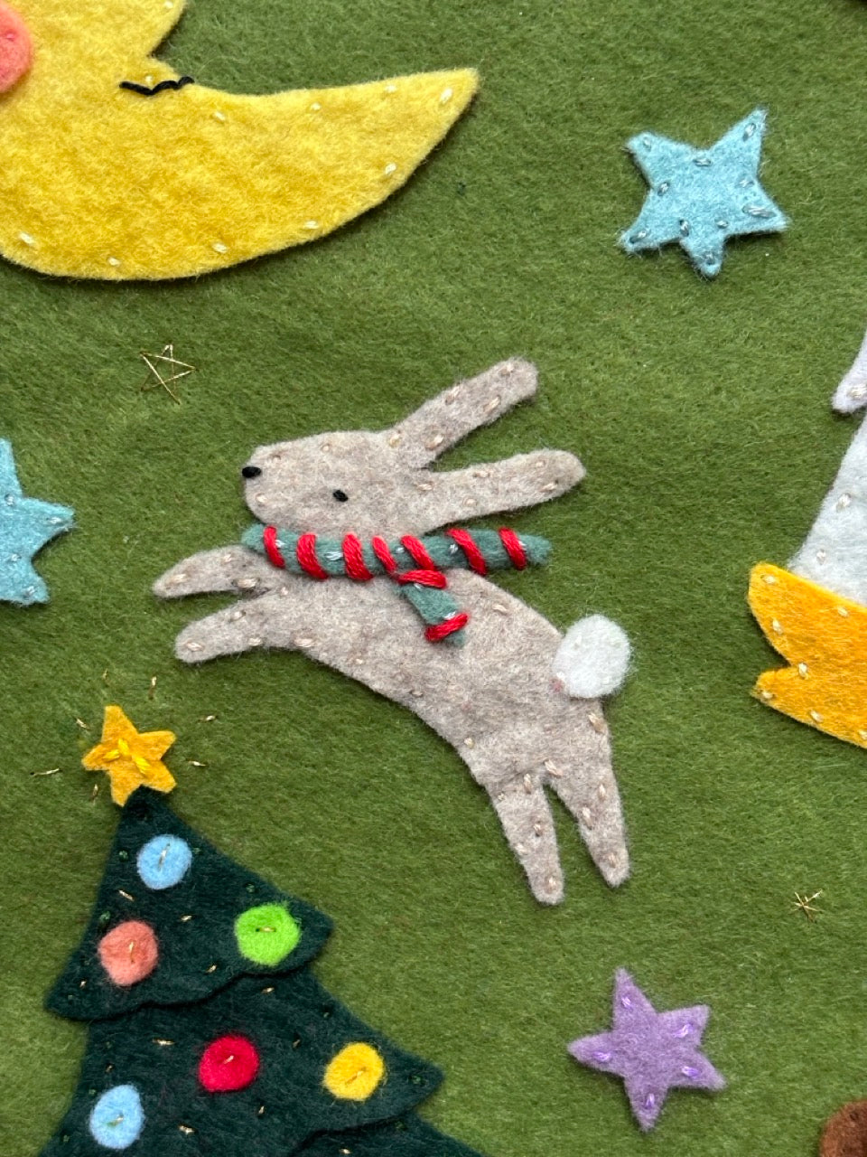 Felt bunny with a scarf, Christmas tree, and stars on a green background