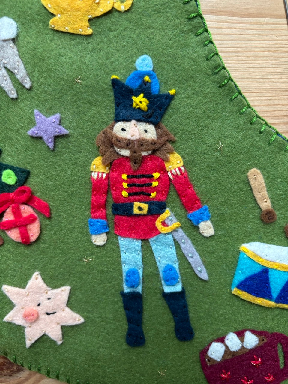 Felt Nutcracker toy on a green felt background with Christmas decorations.