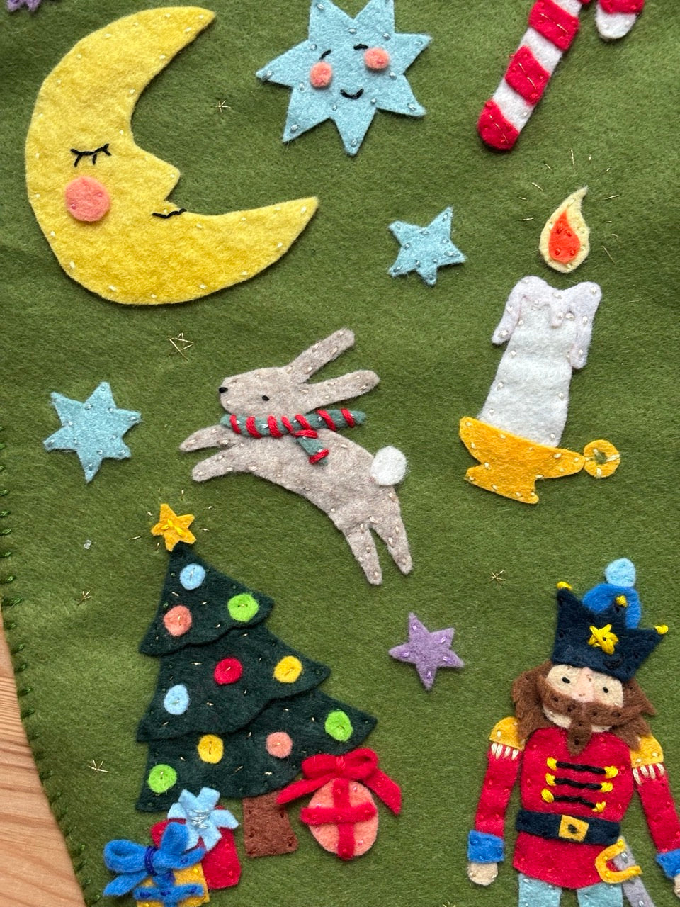 Felt decorations on a green background including a moon, stars, a rabbit, a tree, and a toy soldier.