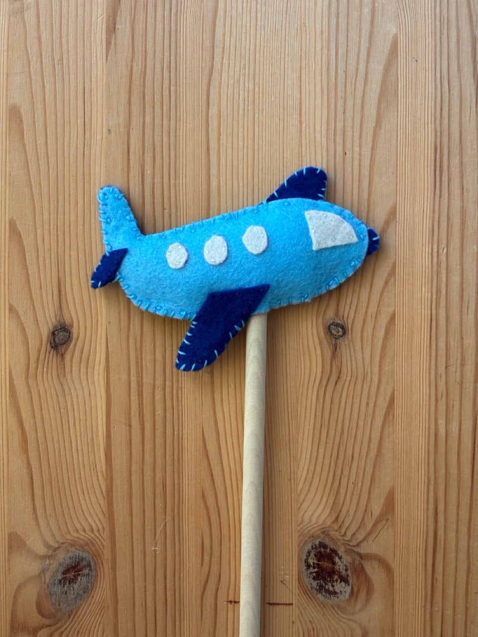 Blue felt airplane toy wand on a wooden surface