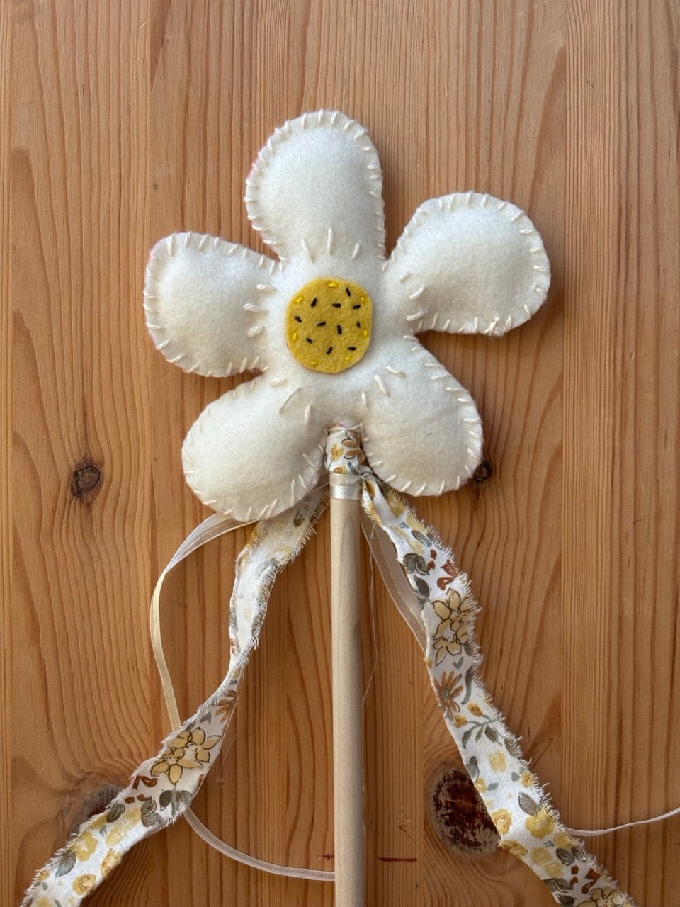 Decorative flower wand with white petals and yellow center on a wooden background