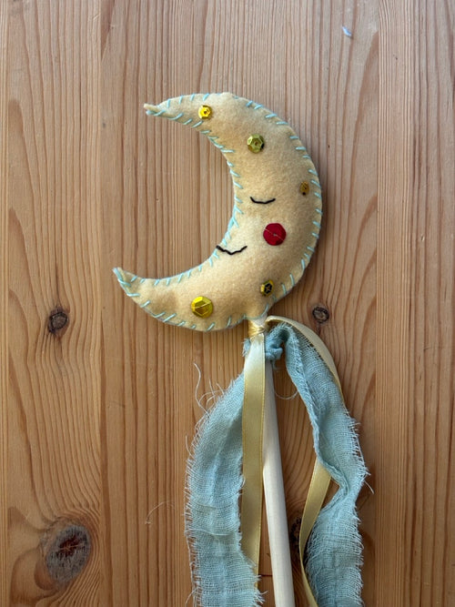 Decorative moon-shaped felt wand with ribbons on a wooden surface