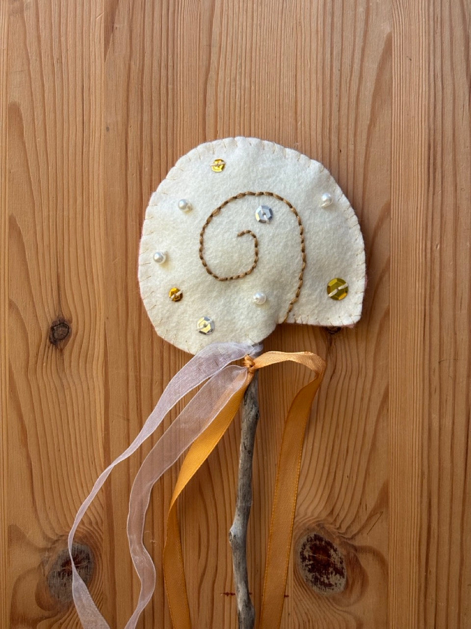 Felt shell wand on a stick with ribbons on a wooden background