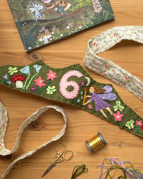 Decorative birthday crown with fairies and flowers on a wooden surface with ribbons and scissors.